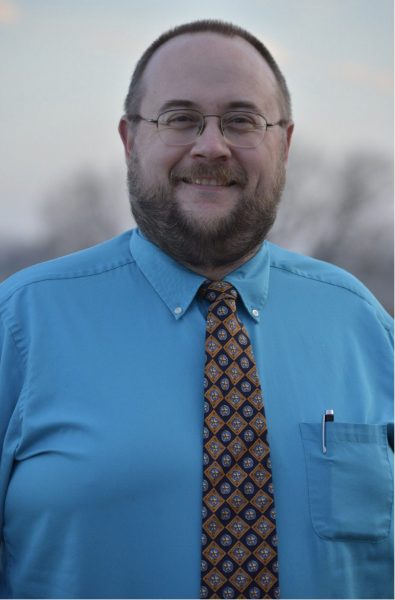 A professional photo of Dr. Derek Everett wearing a tie and blue shirt